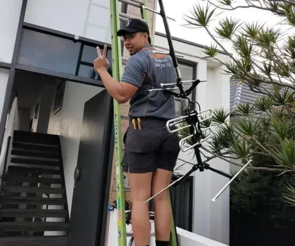 Technician on a ladder providing antenna installation services in Sydney, holding a TV antenna for improved digital TV reception