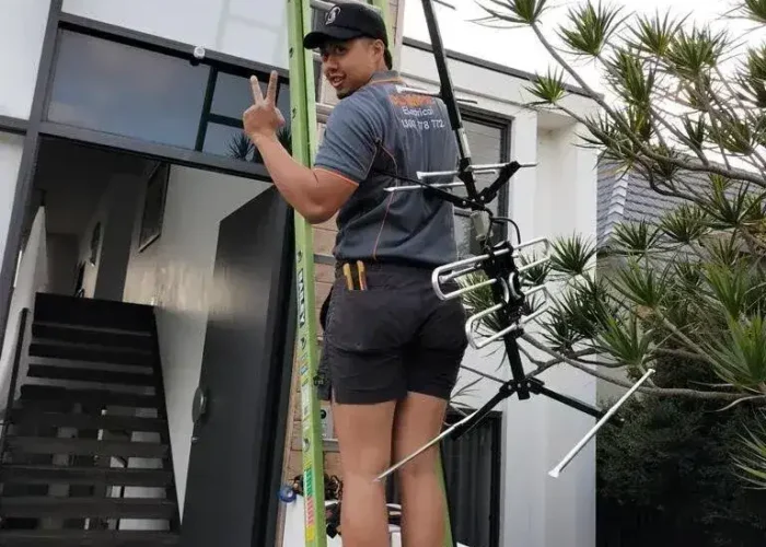 Technician on a ladder providing antenna installation services in Sydney, holding a TV antenna for improved digital TV reception