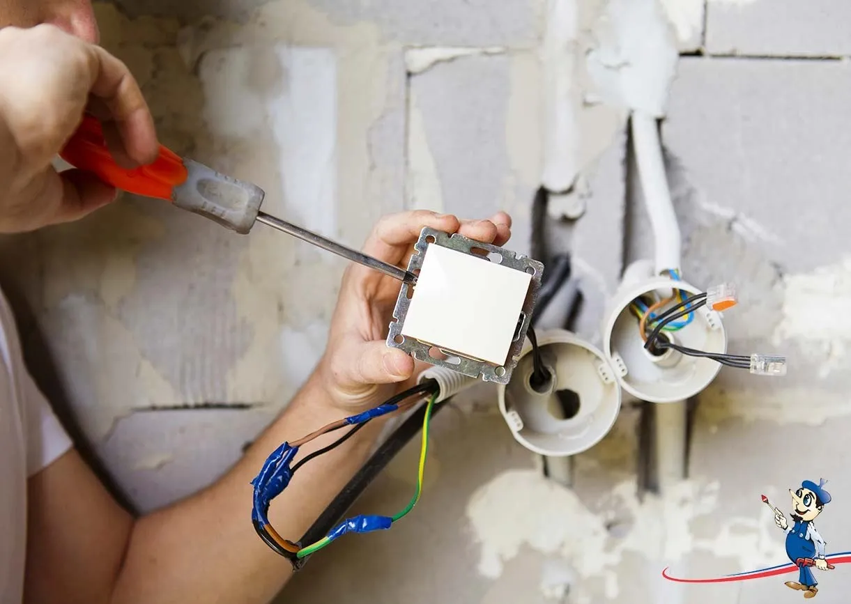 Person using a screwdriver to install a light switch on a wall, with electrical wires exposed and connected in sockets.