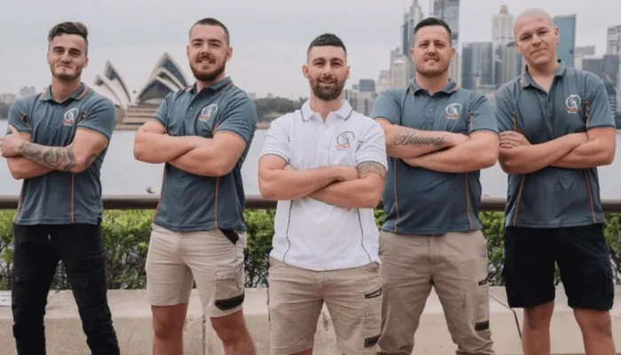 Five men in uniform pose with arms crossed, standing in front of the Sydney Opera House and city skyline. Olympic Electrical electrician on the job